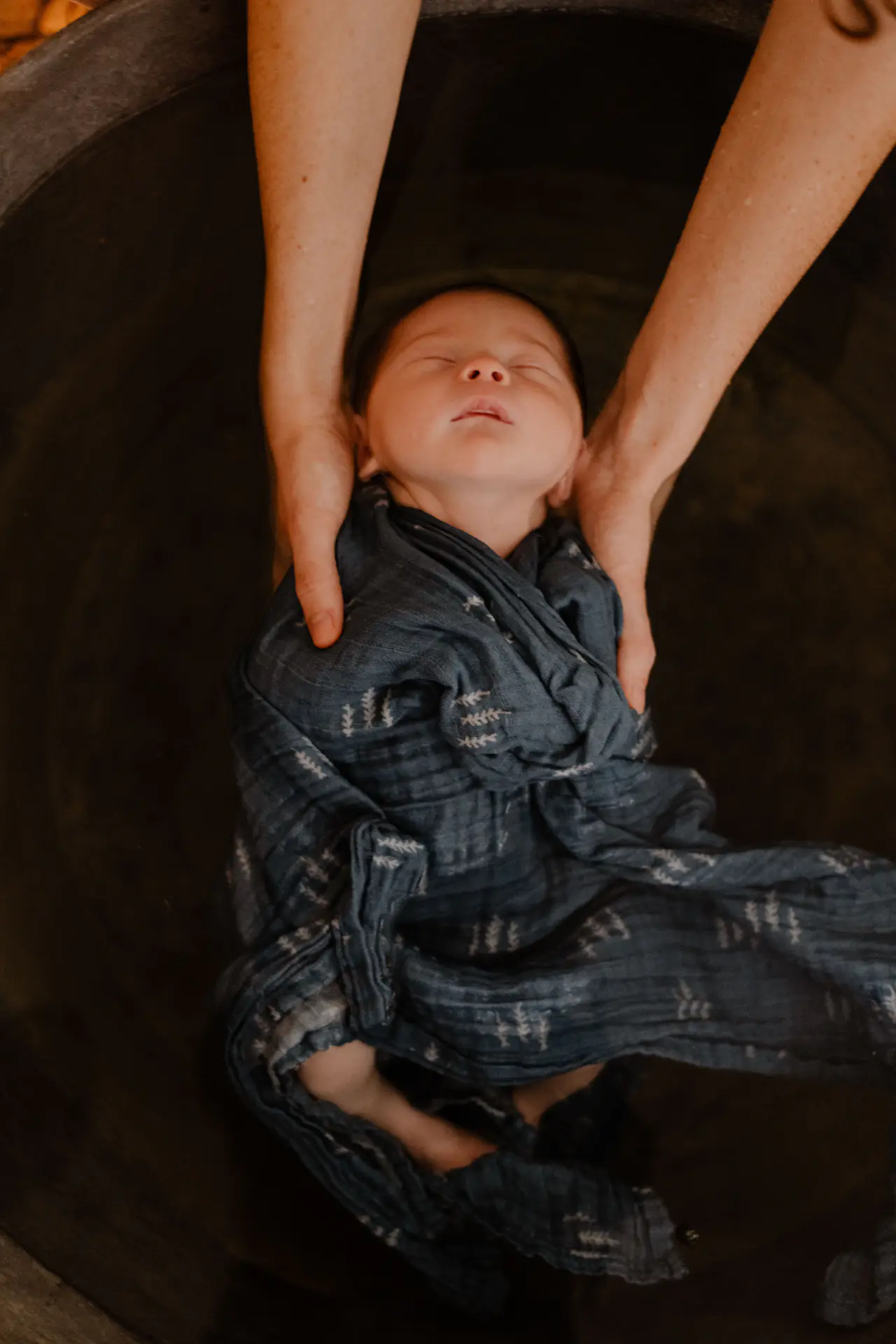 Nouveau-né emmailloté, soutenu par les mains de sa maman dans l'eau du bain